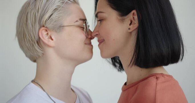 Romantic lesbians with tattoos hug and kiss at home with white walls slow motion close up