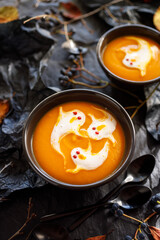 Halloween pumpkin soup decorated with ghosts made of cream in black bowls on a dark decorated background  close up view