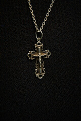 Fototapeta na wymiar Cross on a silver chain, faith, spirituality and religion, dark fabric background.