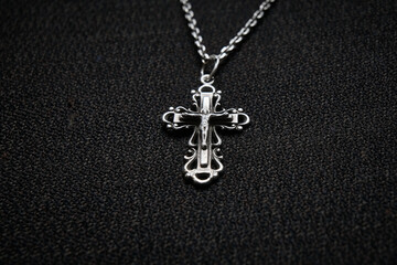 Fototapeta na wymiar Cross on a silver chain, faith, spirituality and religion, dark fabric background.