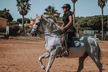 Caballo español en una hipica en andalucia con su Jinete Amazona montandolo con sus riendas y saltando en una pista 