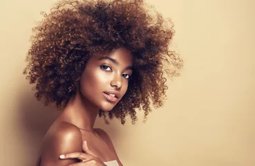 Schöne schwarze Frau. Schönheitsporträt einer afrikanisch-amerikanischen Frau mit sauberer, gesunder Haut auf beigem Hintergrund. Lächelndes schönes Afro-Mädchen. Gelocktes schwarzes Haar © Sofia Zhuravetc