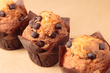 three Chocolate muffins on a brown background.