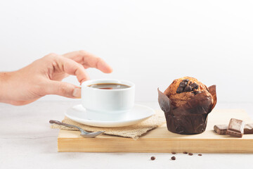 Chocolate muffin, and hand holding a cup of coffee  on wooden board on white background.