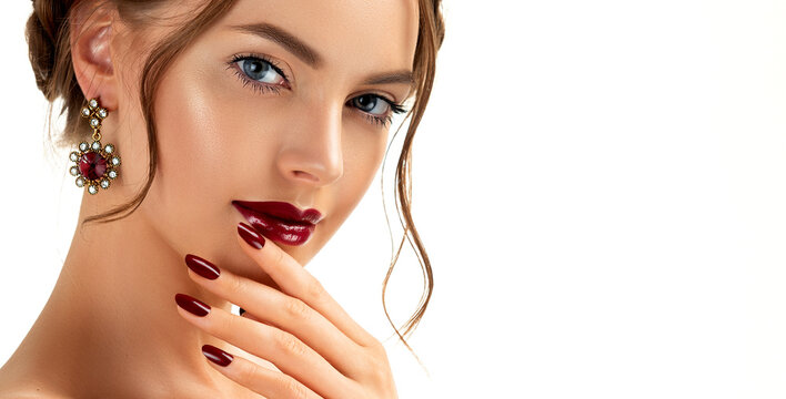 Beautiful model girl with burgundy or wine color manicure on nails . Fashion makeup and cosmetics . Jewelry, earrings and accessories. Beauty woman with braid hairstyle around her head.