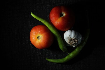 Green chilly, Garlic, Onion, Tomato and Curry leaf are isolated on black background. Ingredients concept. Hot and spicy green chilies and fresh ripe tomato on black background.
