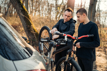 Naklejka premium father and son take the bike down from the rack on the car