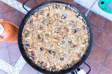 Sartén grande con arroz e ingredientes  en patio trasero.