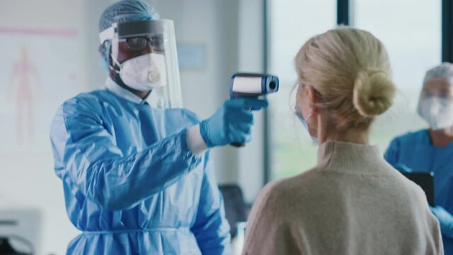 Close Up of Medical Physician in Safety Gear Measuring Senior Female Patient's Body Temperature with Infrared Thermometer in a Health Clinic