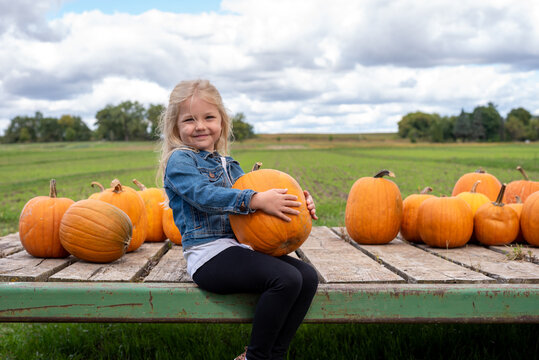 Cute little girl choosing a pumpkin at the farm