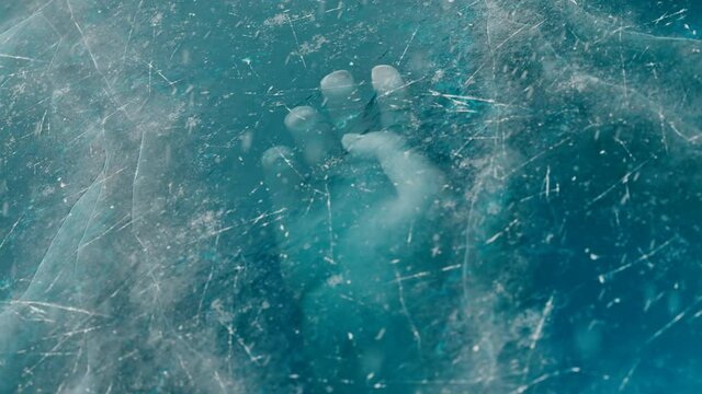 A human hand under the ice. The dead body is trapped underwater below the ice.