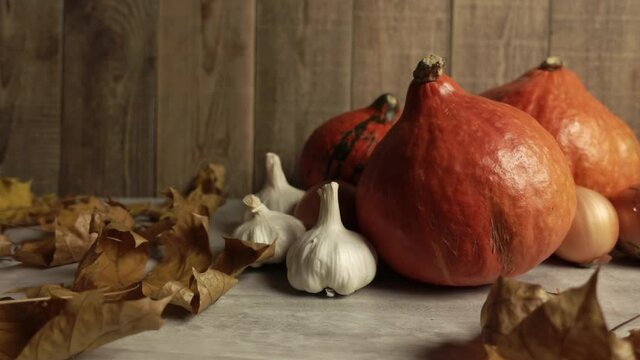 Dry maple leaves are falling at the pumpkins at the wooden table in slow motion. Still life of autumn symbols standing together in a group. The conception of fall harvest celebration and vegetables.