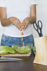Mid section view of a woman dropping carrot slices into a bowl