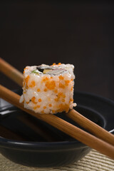 Close-up of a maki sushi with chopsticks on a bowl