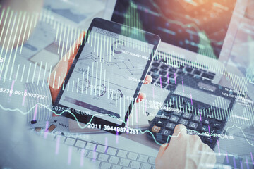 Double exposure of man's hands holding and using a digital device and forex graph drawing....