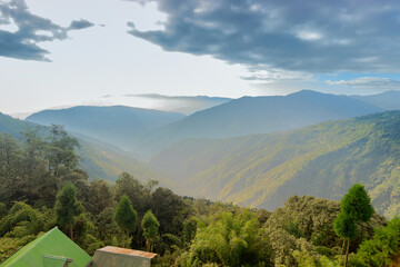 Obraz premium Green valley between Himalayan mountain slopes with tree lines in the foreground, shot with morning mist at Sikkim, India.