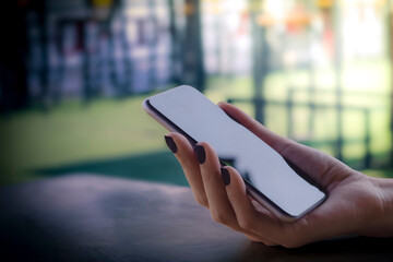Close-up of the hand of a business woman holding a black turned off smartphone. On Blurred gentle artistic nature background and free space for text.