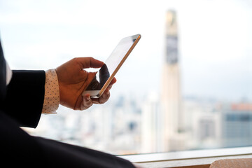 Businessman use smartphone for reading news in mobile seem alone relaxing near bangkok tower building window view at modern office in sunny day, Social media for using smart phone concept