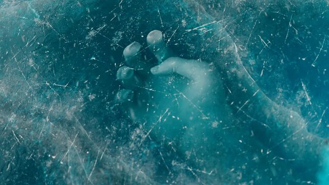 A human hand under the ice. The dead body is trapped underwater below the ice.