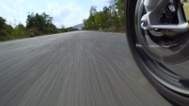 Motorcycle ridind on a road in nature. Close up wheel on a bumpy asphalt road.