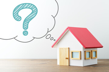 House and question. Miniature house and illustrations question mark in balloon. Wood desk and white...