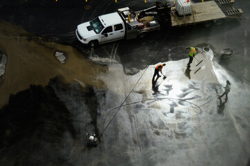 Personas limpiando el piso junto a una van blanca, piso mojado y reflejo de luz solar