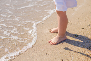 Small baby feet close-up on the sand of the sea beach. Sea water washes the feet. Happy childhood. Rest at the sea. Summer sunny day. Copy space.