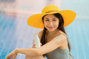 Attractive asian woman in yellow hat with healthy skin applying sunscreen standing outdoors on a sunny day.
