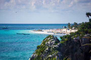 The turquoise waters of the Caribbean wash against white sand beaches and rocky cliffs at Tulum beach near ancient Mayan ruins on the coast of Mexico.