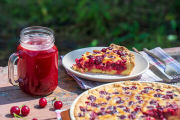 Homemade cherry pie and red cherry drink on the wooden table in garden