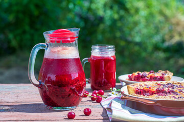 Homemade cherry pie and red cherry drink on the wooden table in garden