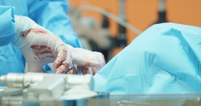 First plan blurred - focused surgery drill on sterilization containers with sterilized tools. Closeup focused hands of male veterinarian, in white gloves and in surgical outfit, while he is operating