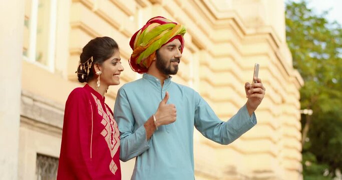Hindu woman with dot on forehead and man in turban standing outdoor and talking via webcam on smartphone. Videochat. Male and female videochatting on mobile phone. Fast video connection. Call.