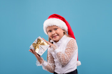 Waist up portrait of a little smiling blonde girl  with Sante Claus's cap holding a gift box