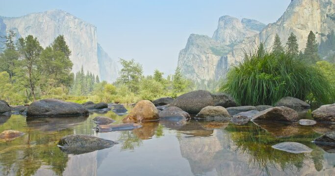 Cinematic landscape and mountains view. Static shot of Yosemite valley in light morning mist. Beautiful reflection of sheer cliffs in the pond with still water. Scenic nature background on sunny day