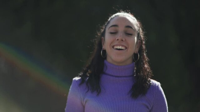 Portrait of a happy young woman laughing outdoors with rainbow colors as lens flare. Face expressions