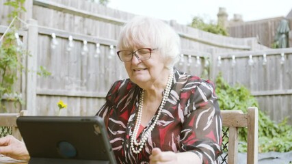 Elderly Woman talking on Skype on a tablet device laughing in the garden day
