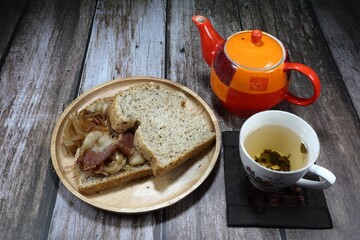 Famous local breakfast menu set, sliced bread with roasted bacon and onion on the wooden plate serving with hot tea. Mock up food in the morning.