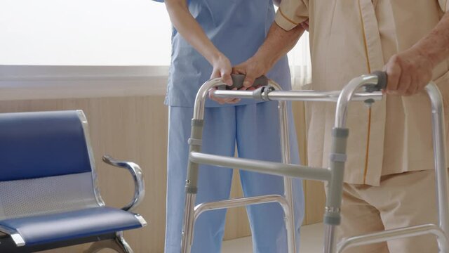 Close up attractive young asian woman or nurse take care senior old man on cane or walker feeling helpful and empathy at nursing home or hospital hallway. Hip, knee and leg problem in older people.