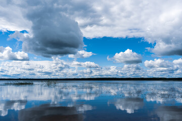 Fototapeta na wymiar The lake's mirrored surface reflects lush beautiful blue sky with clouds