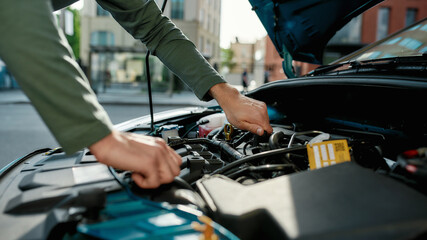 Close up of hands of young man examining broken down car engine, standing near his car with open hood on the city street