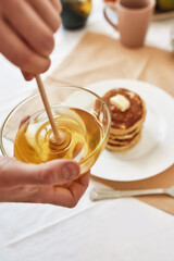 Close up of hands holding a bowl with honey, A stack of sweet tasty pancakes on the table, Process of preparing breakfast