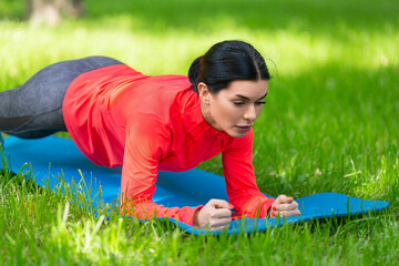 Fototapeta na wymiar Woman doing plank exercise on a grass in city park. Closeup.