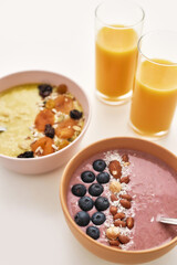 Close up of smoothie bowl with fresh berries, nuts and orange juice in glass isolated over white background