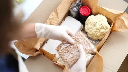 A female volunteer puts food in a box. Courier delivery of groceries. Helping people in need.