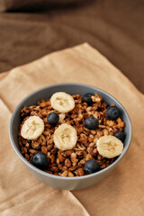 Close up of homemade granola in a plate with nuts, honey, blueberries, banana and other natural ingredients served on napkin over brown background