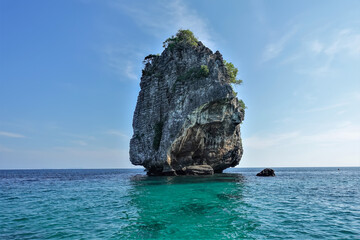 A small uninhabited island in the Andaman Sea against the background of blue sky. A conical rock with steep slopes, few trees at the top. Turquoise water around. Thailand
