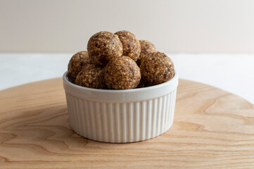 Homemade energy truffle balls in white bowl on wooden board. Raw vegan healthy dessert, date and...