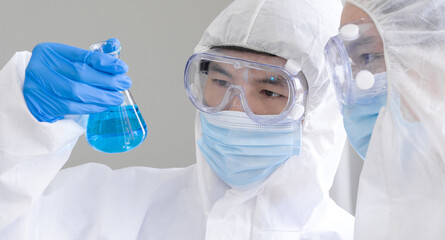 Two Scientists discuss about blue liquid chemical in Erlenmeyer flask.