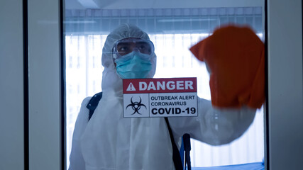 Worker in personal protective equipment (ppe) suit cleaning in building with spray disinfectant water to remove covid 19